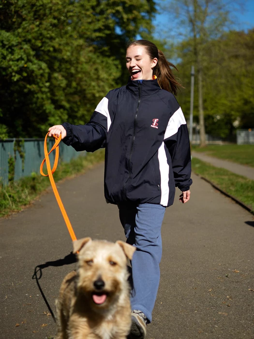 A smiling walker in a park, orange Dog-Out! leash in hand